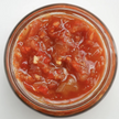 A jar of sweet chilli jam with visible pieces of red pepper and garlic.