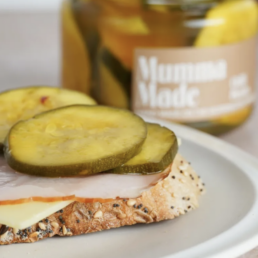 Sandwich with pickles and ham on a plate with a jar of pickles in the background.