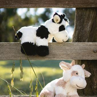 Two plush cow toys on a wooden fence with a natural background