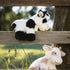 Two plush cow toys on a wooden fence with a natural background