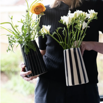 Person holding two striped vases or water jugs with flowers indoors